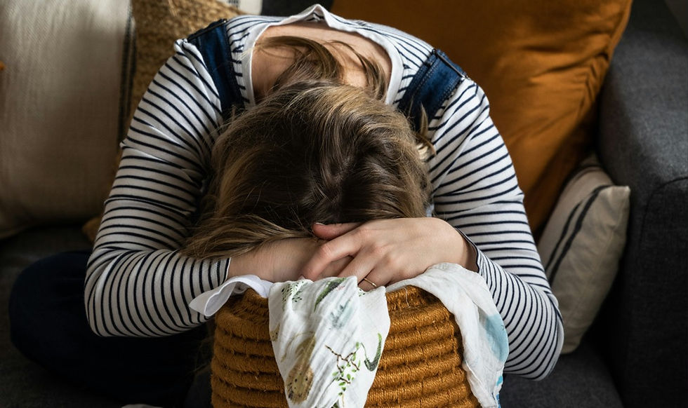 Woman in a striped shirt hugs a child with head down on a couch, surrounded by cushions, in a quiet, comforting scene.