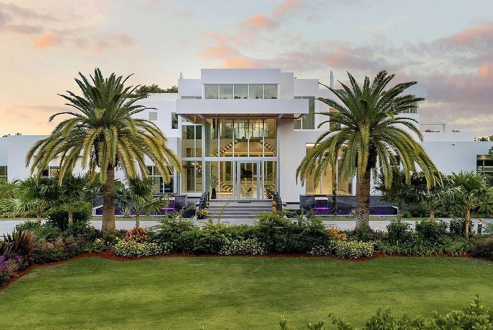 Modern white mansion with large glass windows, surrounded by palm trees and lush gardens, at sunset with a serene atmosphere.
