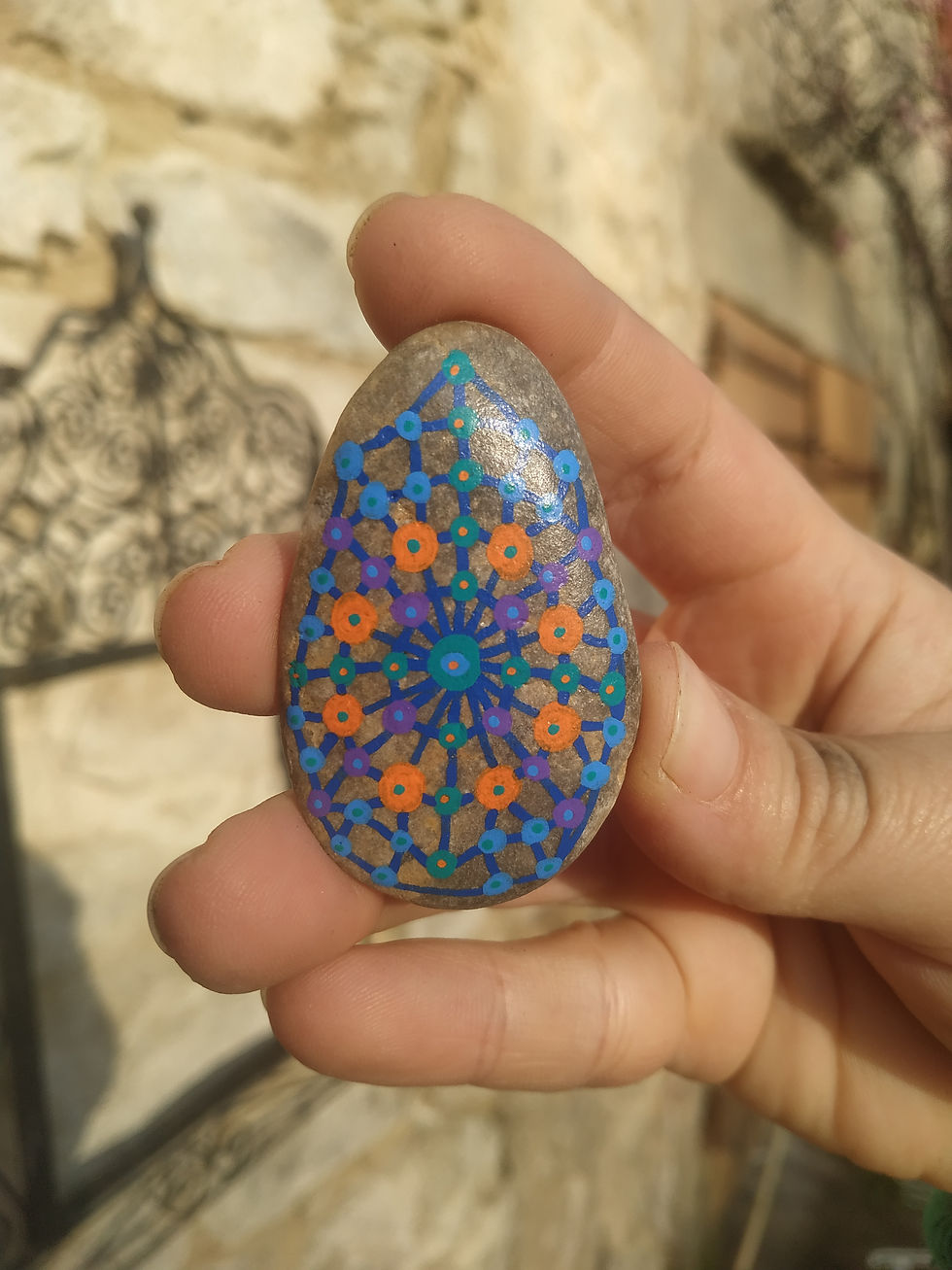 Peinture sur galet vibratoire par Oréalys Révayia, tenue dans la main, éclairée par le soleil, énergie spirituelle.