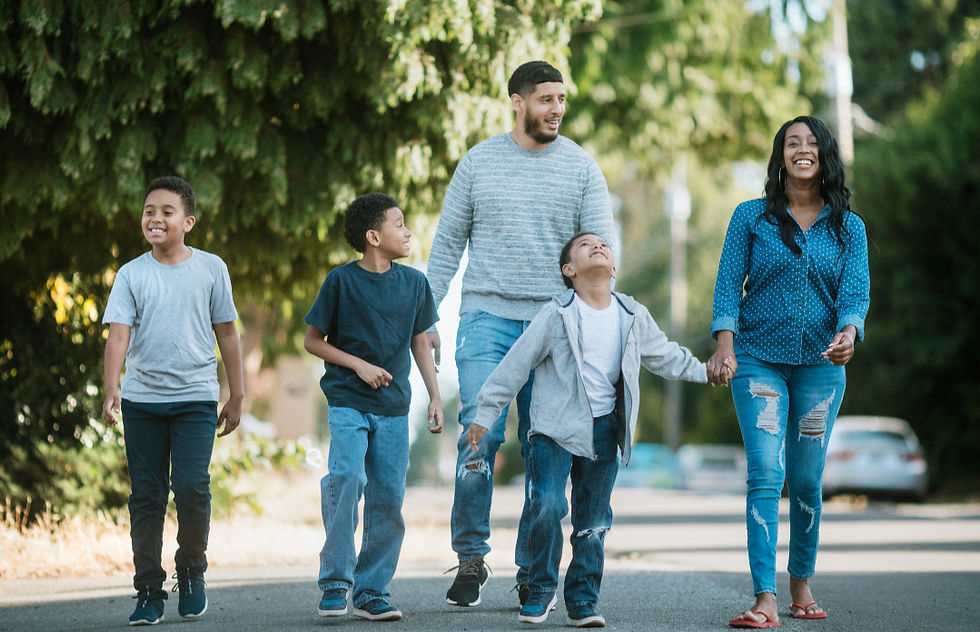 A family of five walks down a tree-lined street, smiling and holding hands. Casual wear, bright day, joyful mood.