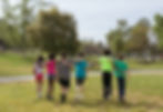 Six kids walk with arms around each other in a sunny park, surrounded by green trees and grass, creating a mood of friendship and joy.