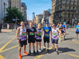 Runners posing in a city street before a race, wearing colorful bibs and running attire | NKMT