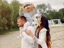 Young girl riding on her fathers shoulders with her mother's hat as she walks by their side
