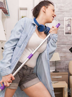 Teen girl with headphones around her neck using a mop as a microphone singing into it