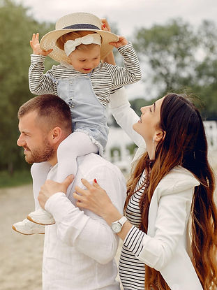 Young girl riding on her fathers shoulders with her mother's hat as she walks by their side