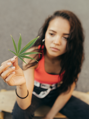 teen girl sitting on a skateboard holding a cannabis leaf