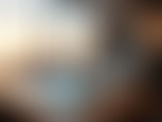 Astronauta em traje espacial sentado à mesa, observando uma projeção holográfica de uma cidade. Ao fundo, uma ampla janela mostra o horizonte urbano durante o entardecer.