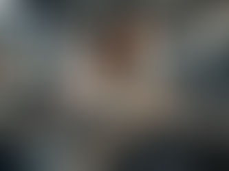 Astronauta em uma oficina examinando minuciosamente uma peça mecânica com uma lupa. O capacete está sobre a bancada ao lado.