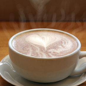 A warm cup of coffee topped with soft foam shaped like a heart, resting on a saucer, evoking a quiet morning ritual.
