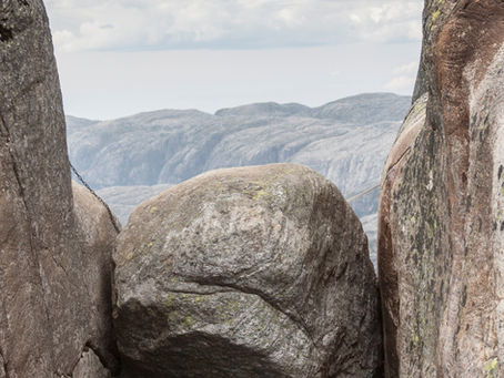 Gros rocher coincé entre deux parois rocheuses abruptes, avec un paysage montagneux et un horizon dégagé en arrière-plan, symbolisant le sentiment d’être pris·e et la possibilité d’une issue malgré l’enfermement apparent.