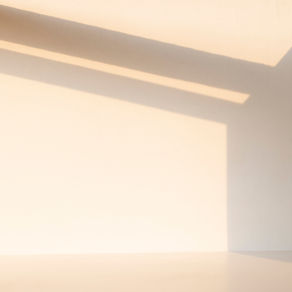Un espace intérieur minimaliste où la lumière du soleil projette des ombres géométriques sur un mur et le sol.