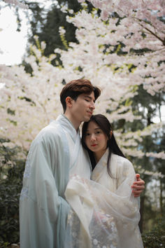 Kita Studios pre-wedding photography: A couple embracing during a cherry blossom photoshoot. The image features a whimsical, fairytale aesthetic with natural lighting and romantic spring blooms in the background.