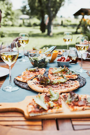 Dinner in a home garden. Pizza, salads, fruits and white wine on table in a orchard in a b
