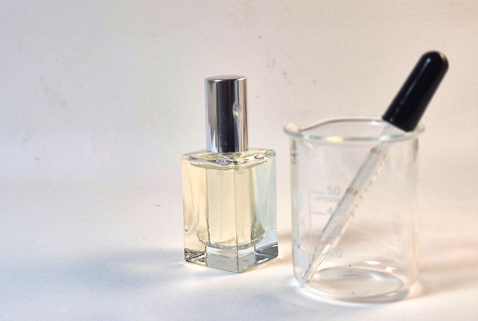 Perfume bottle with silver cap beside a beaker holding a dropper. Set against a neutral background, creating a clean, lab-like feel.