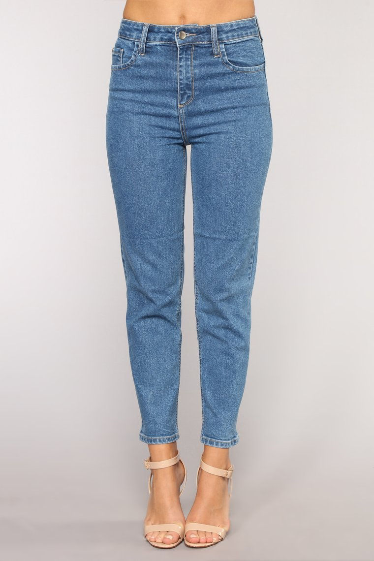 Miniatura: Piernas de mujer vistiendo jeans azules ajustados sobre fondo gris claro.