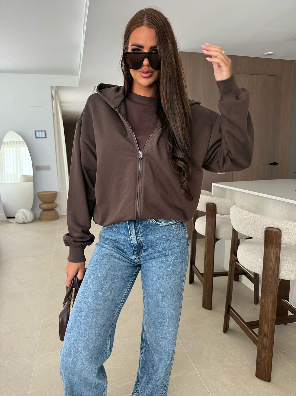 Miniatura: Mujer con sudadera marrón oversize, jeans anchos y gafas de sol.