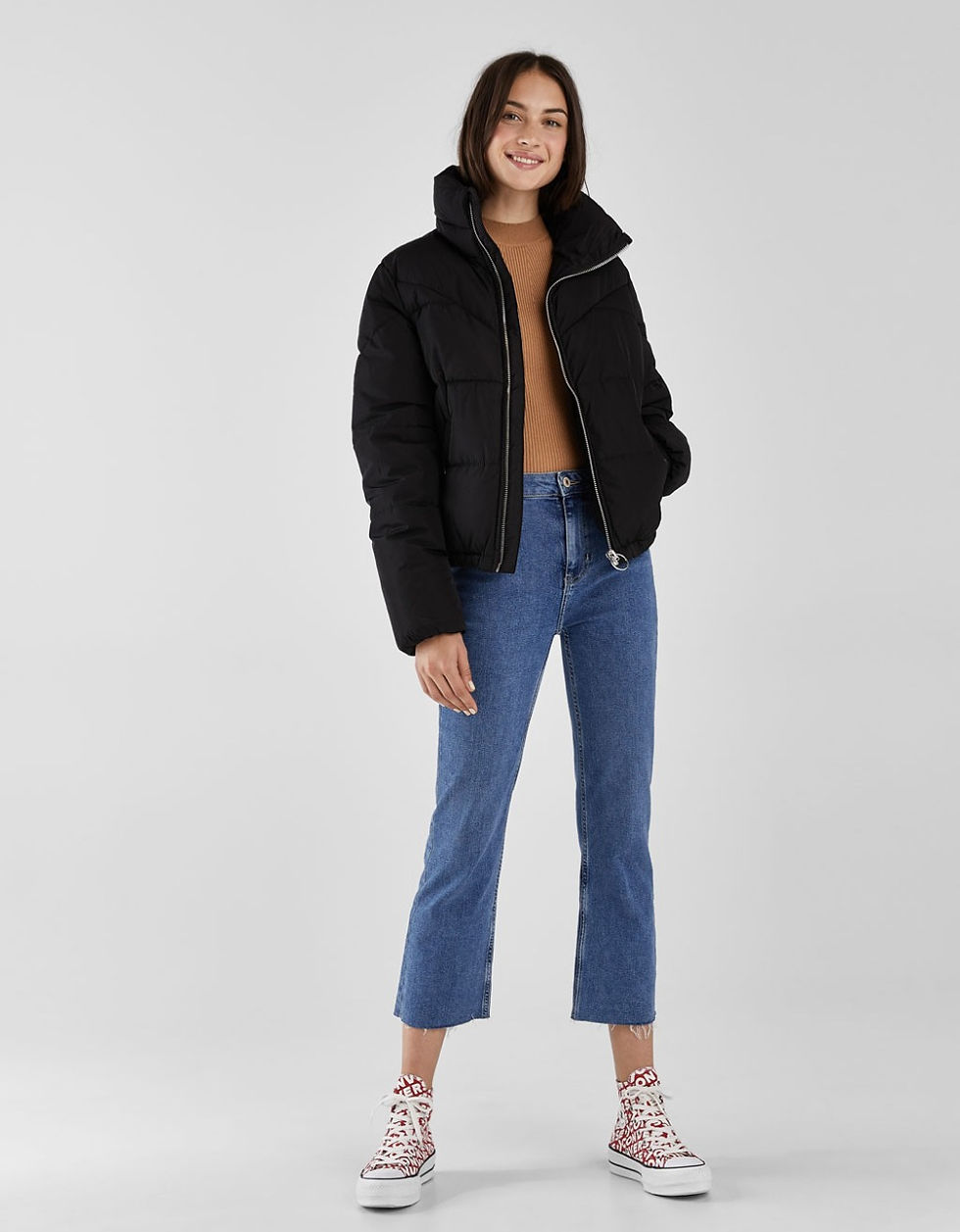 Miniatura: Mujer sonriente luciendo campera puffer negra y jeans azules casuales.