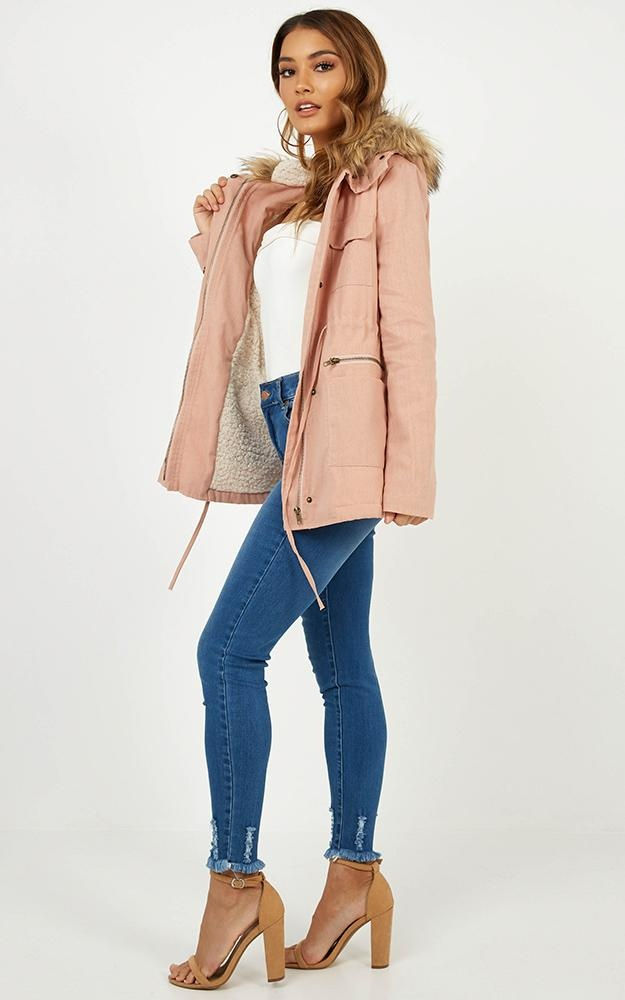 Miniatura: Mujer de pie con chaqueta rosa pálido y jeans ajustados azules.