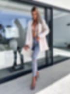 Mujer rubia elegante posa con blazer blanco, jeans y tacones altos.