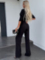 Mujer rubia de espaldas posando con elegante mono negro y bolso.