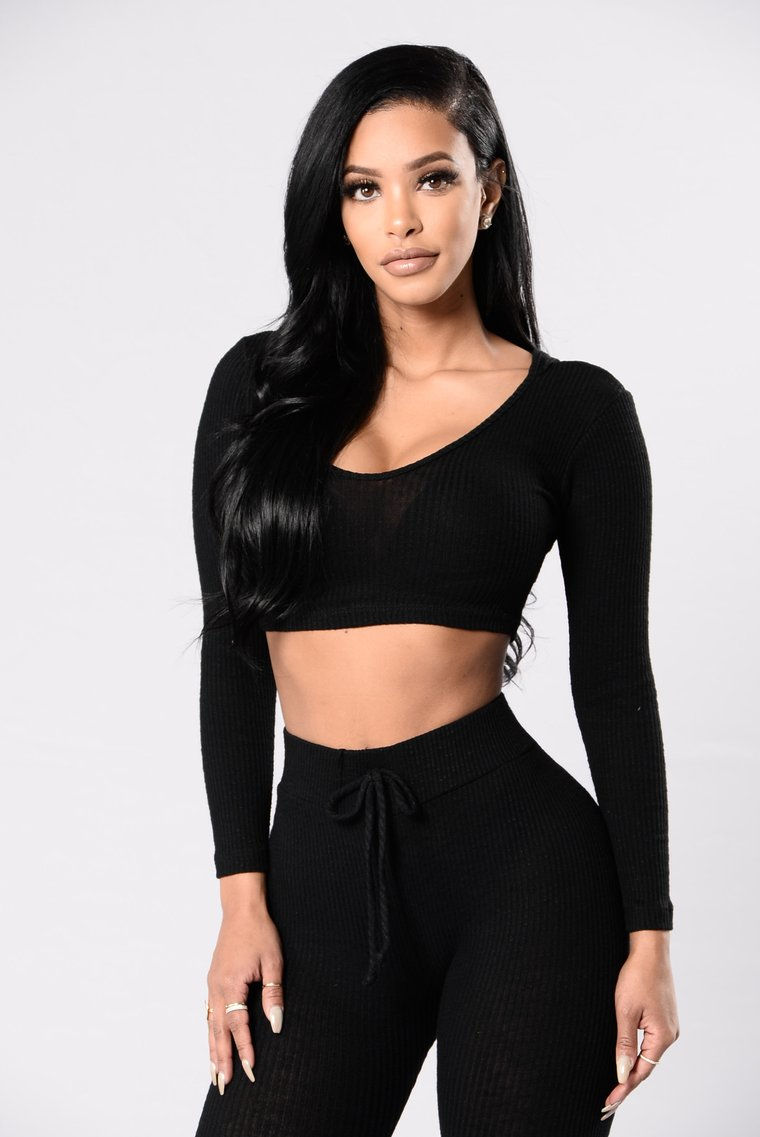 Miniatura: Mujer joven modelando crop top negro ajustado de manga larga escote V.