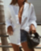 Mujer vistiendo camisa blanca suelta, shorts denim y bolso negro.