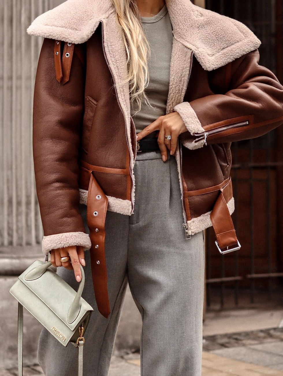 Miniatura: Mujer vistiendo chaqueta aviador marrón forrada, pantalón gris y bolso verde.