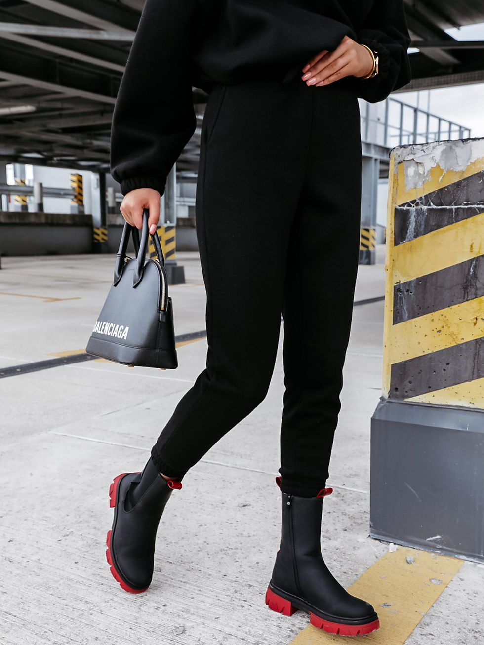 Miniatura: Mujer con pantalones negros, botas y bolso Balenciaga en estacionamiento.