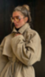 Mujer elegante con chaqueta beige moderna y gafas aviador amarillas.