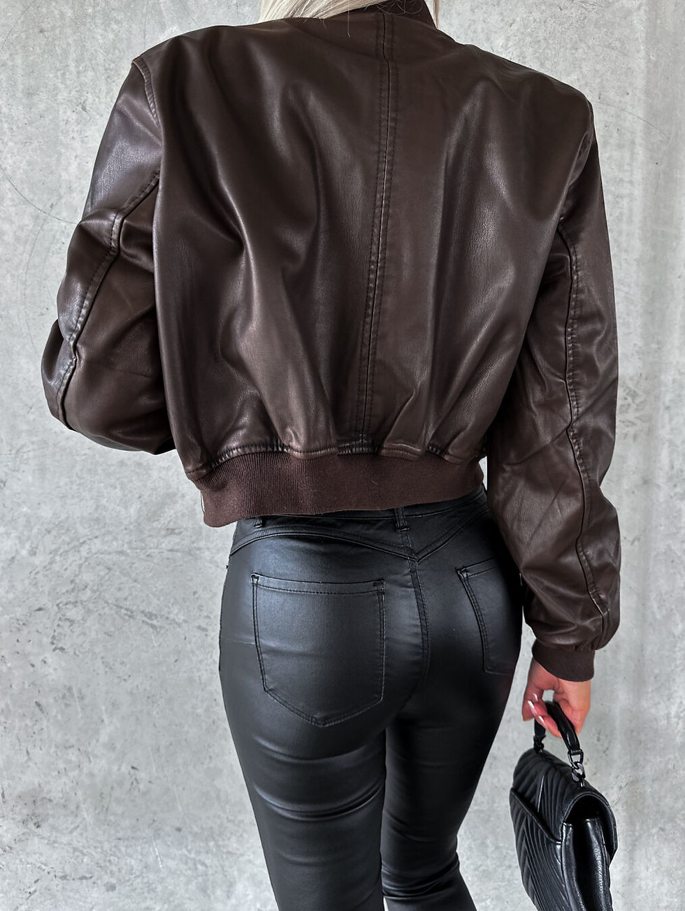 Miniatura: Mujer de espaldas con chaqueta de cuero marrón y pantalones ajustados negros.