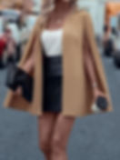 Mujer elegante con blazer capa camel, falda, sosteniendo bolso y café.