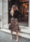 Mujer elegante con top negro, falda plisada estampado leopardo, estilo urbano.