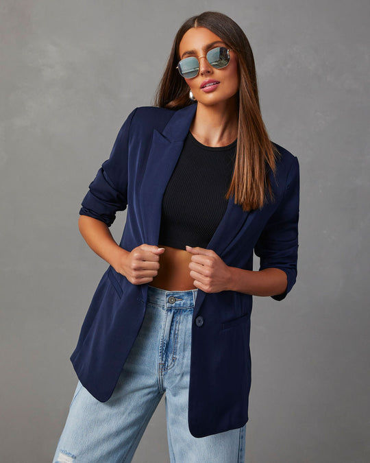 Miniatura: Mujer elegante con blazer azul marino, top negro y jeans claros.