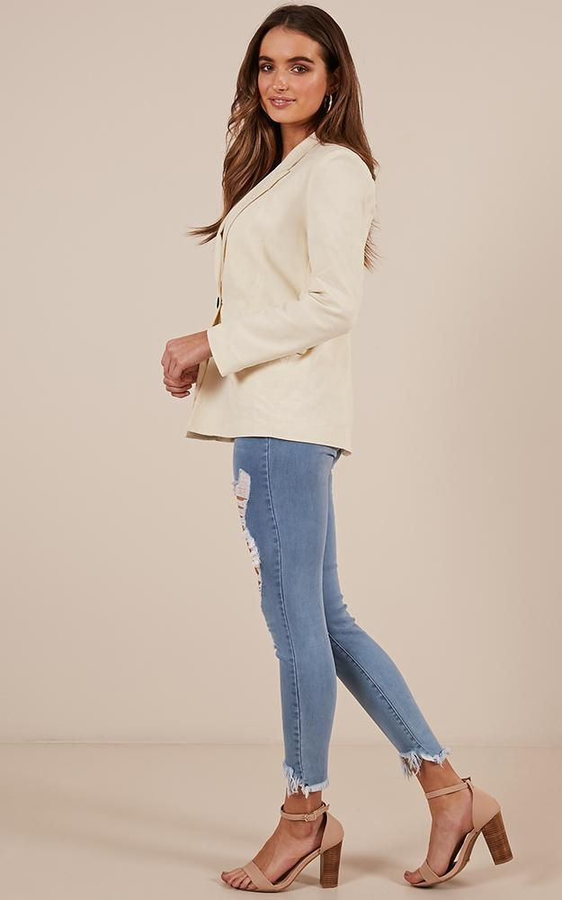 Miniatura: Mujer de perfil luciendo blazer crema y jeans rotos ajustados.