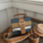 Striped blue, tan, white handbag with gold buckle and brown leather strap.