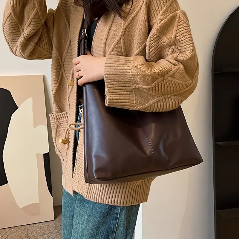 Thumbnail: Person in brown cardigan and jeans holding a dark brown shoulder bag.