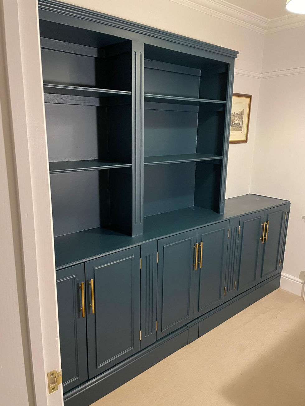 Custom built-in storage unit painted dark teal with brass handles—open shelving above and Shaker-style cupboards below