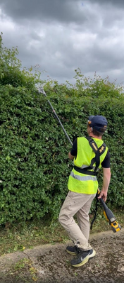 Reigate Handyman in hi-vis using a cordless long-reach hedge trimmer with harness and safety goggles