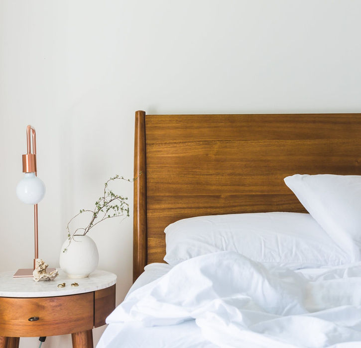 White bedding on a wooden bed frame with a bedside table and lamp