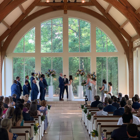Wedding ceremony with couple exchanging vows in front of guests in a chapel with large windows.