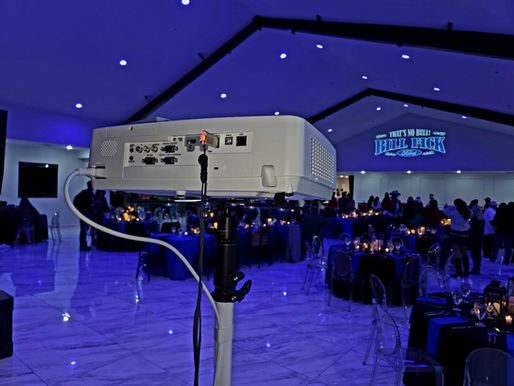 Corporate event logo projection and blue uplighting over banquet tables at a Houston venue, by AMP Events and Lighting