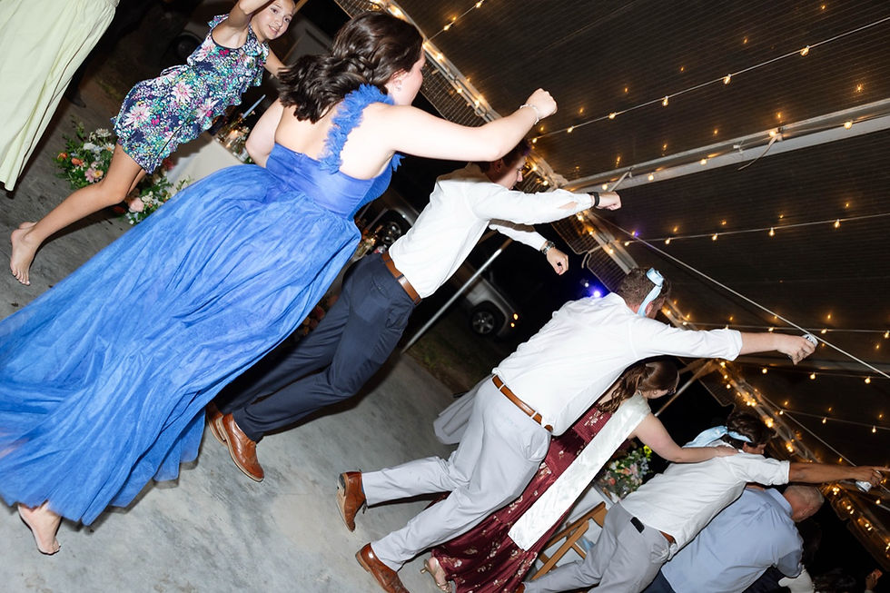 Guests in formal dresses jumping and dancing on a packed dance floor at night under string lights