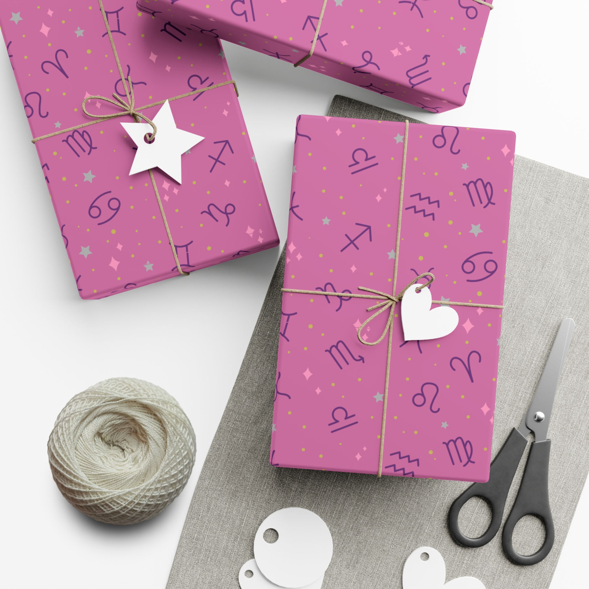 Wrapped gifts on pink paper, zodiac symbols, twine, and scissors on white background.