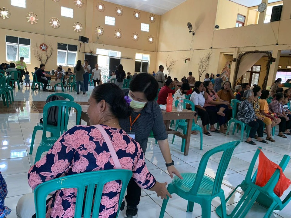 People at an event, many sitting in green chairs, socializing indoors background.