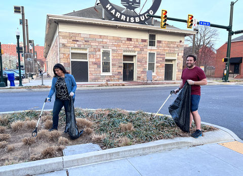 Two people picking up trash in front of the Broad Street Market
