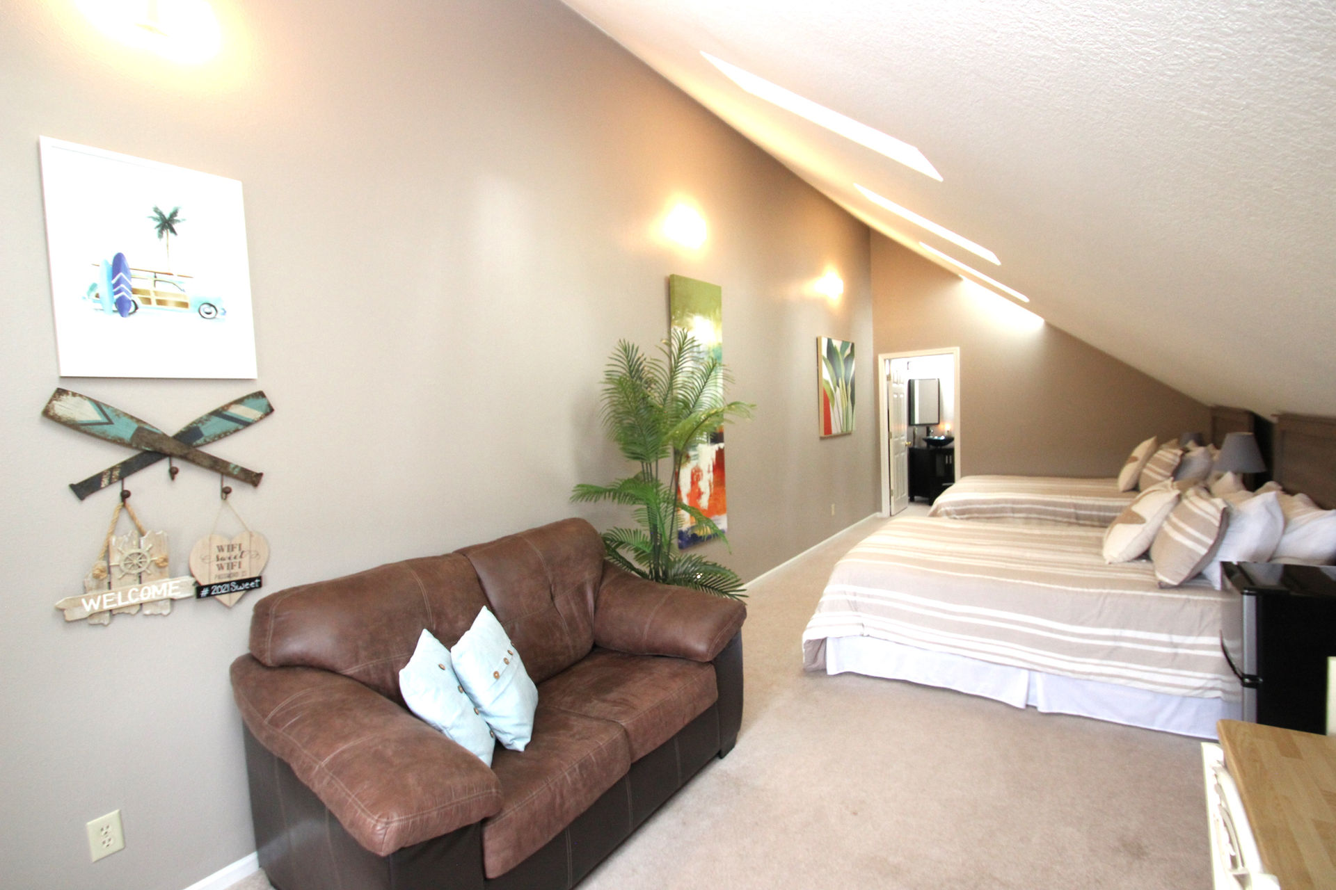 Cozy living space with brown sofa, artwork, plants, and two beds. Beach Loft