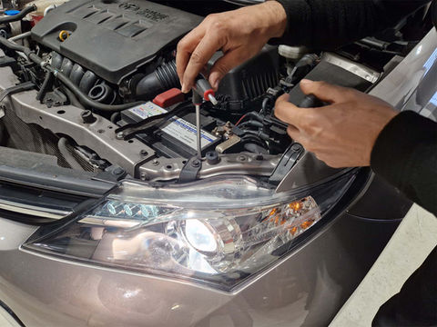 Automechaniker mit Schraubenzieher bei geöffneter Autohube