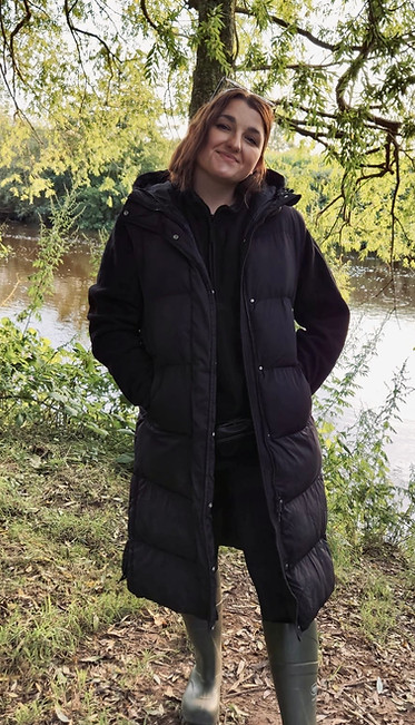 Emily Macaulay smiling stood by a river in the autumn