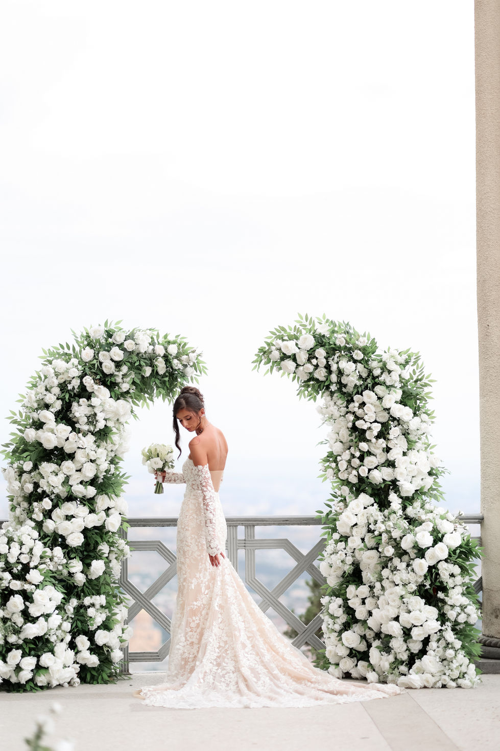 Beautiful bride posing beneath a white flower arch during her wedding photoshoot.