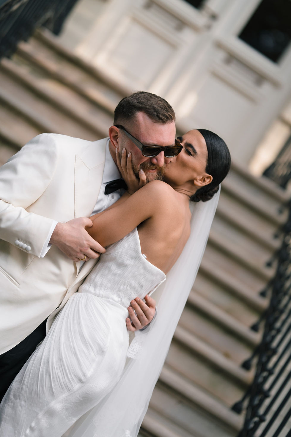 Bride kissing groom on cheek, both in formal attire.